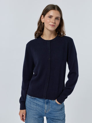 Woman wearing a navy cardigan and blue jeans against a light gray background Navy