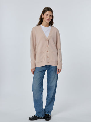 Woman wearing a beige cardigan, white shirt, blue jeans, and black shoes on a white background Sunkissed