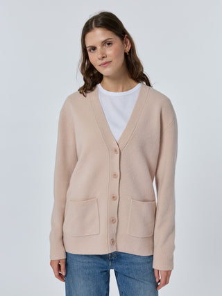 Woman wearing a beige cardigan over a white shirt on a light gray background Sunkissed