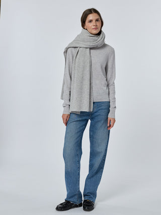 Person wearing a gray sweater, scarf, and blue jeans on a white background Smoke