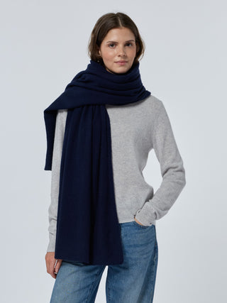 Woman wearing a navy scarf, gray sweater, and blue jeans on a light gray background Navy