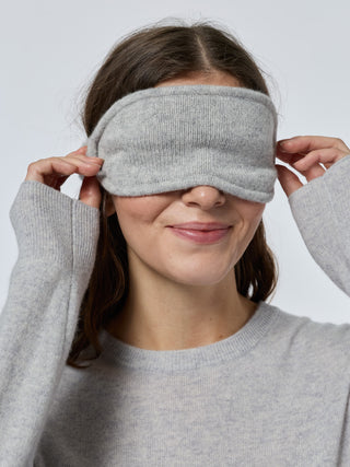 Person wearing a gray knit eye mask against a plain background smoke