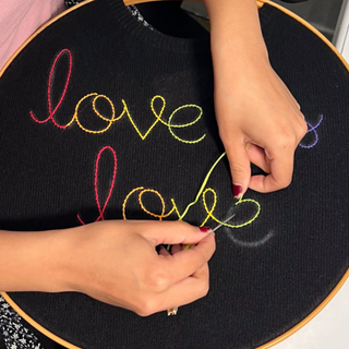 Person embroiderying the word 'love' on a black fabric with colorful thread.